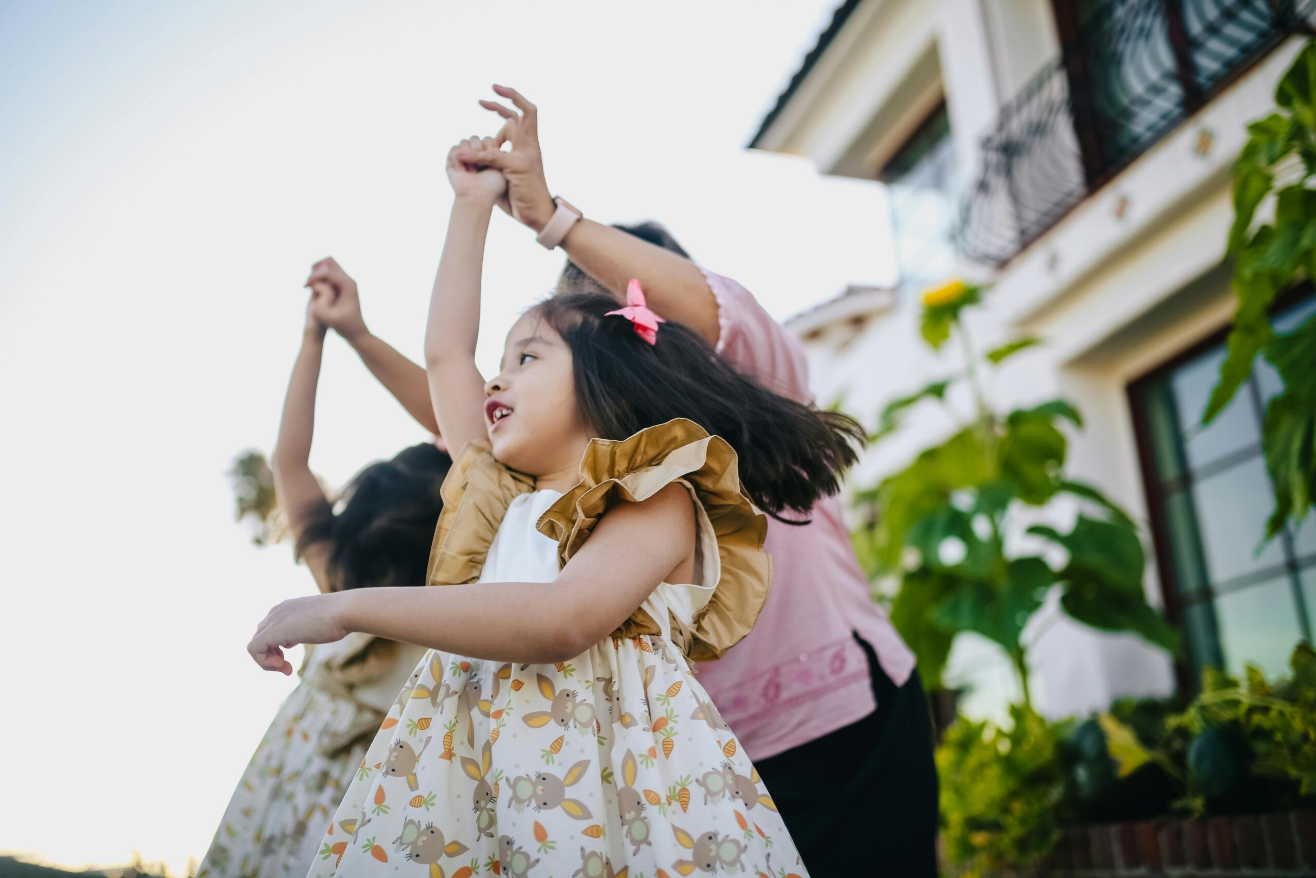 A joyful moment of a mother and her daughters dancing and playing outside on a sunny day.